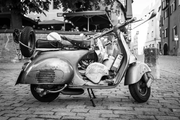 Eine alte Vespa mit einem Reservereifen am Gepäckträger und einem alten Helm im Einstieg, aufgenommen in Italien